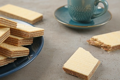 Photo of Plate of delicious wafers with cup of drink on grey stone background, closeup