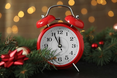 Photo of Alarm clock with decor on black table against blurred Christmas lights, closeup. New Year countdown