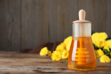 Jar with organic honey and chrysanthemum flowers on wooden table. Space for text