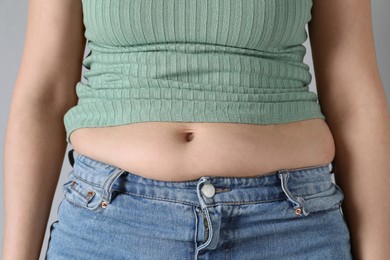 Photo of Woman wearing tight clothes on light grey background, closeup. Overweight problem