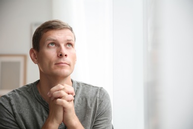 Photo of Man with hands clasped together for prayer near window. Space for text