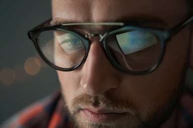 Photo of Young man wearing glasses on blurred background, closeup. Ophthalmology service