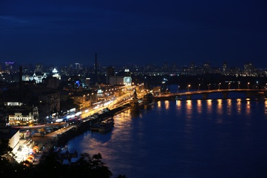 KYIV, UKRAINE - MAY 21, 2019: Beautiful view of night cityscape with illuminated buildings near river and bridge