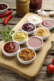 Photo of Different tasty sauces in bowls and ingredients on wooden table