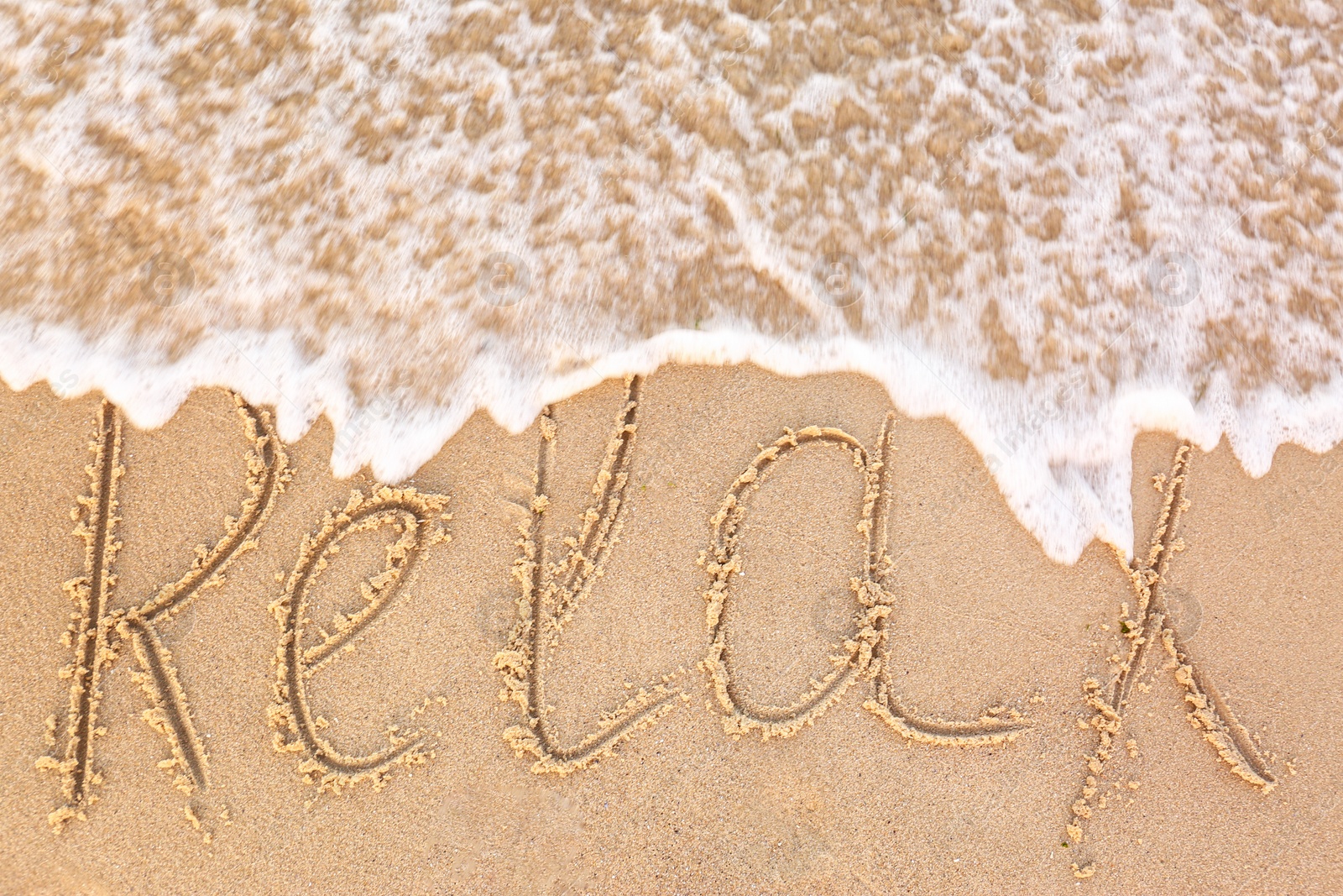 Photo of Word "RELAX" written on sandy beach and sea wave, top view