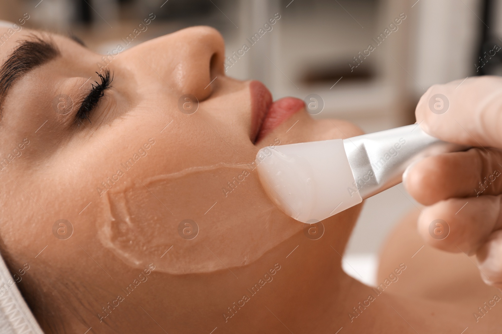 Photo of Young woman during face peeling procedure in salon, closeup