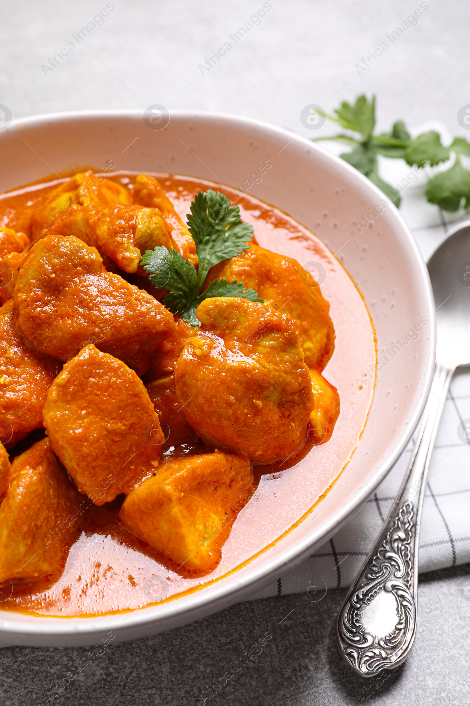 Photo of Bowl of delicious chicken curry on light grey table, closeup