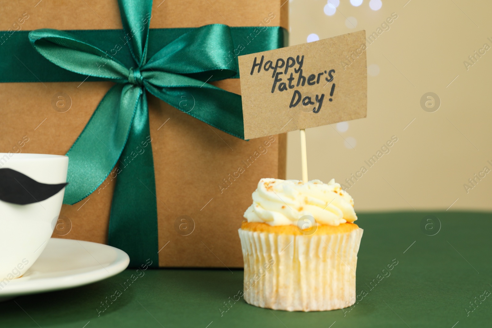 Photo of Happy Father's Day. Tasty cupcake with greetings and gift box on green table, closeup