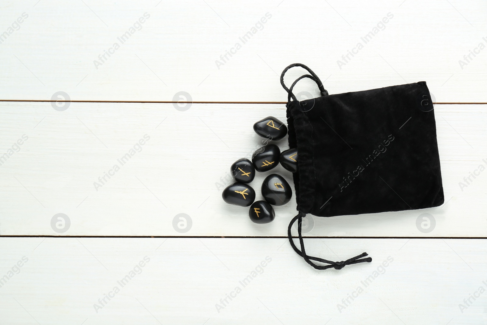 Photo of Bag with black rune stones on white wooden table, flat lay. Space for text