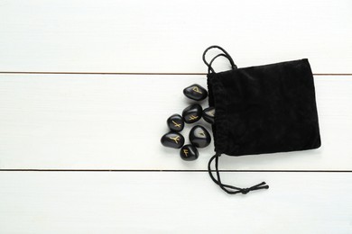 Photo of Bag with black rune stones on white wooden table, flat lay. Space for text