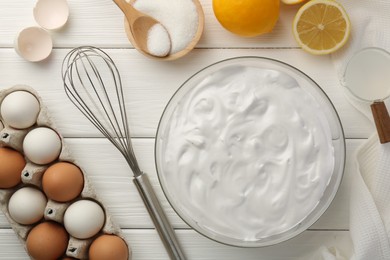 Bowl with whipped cream, whisk and ingredients on white wooden table, flat lay