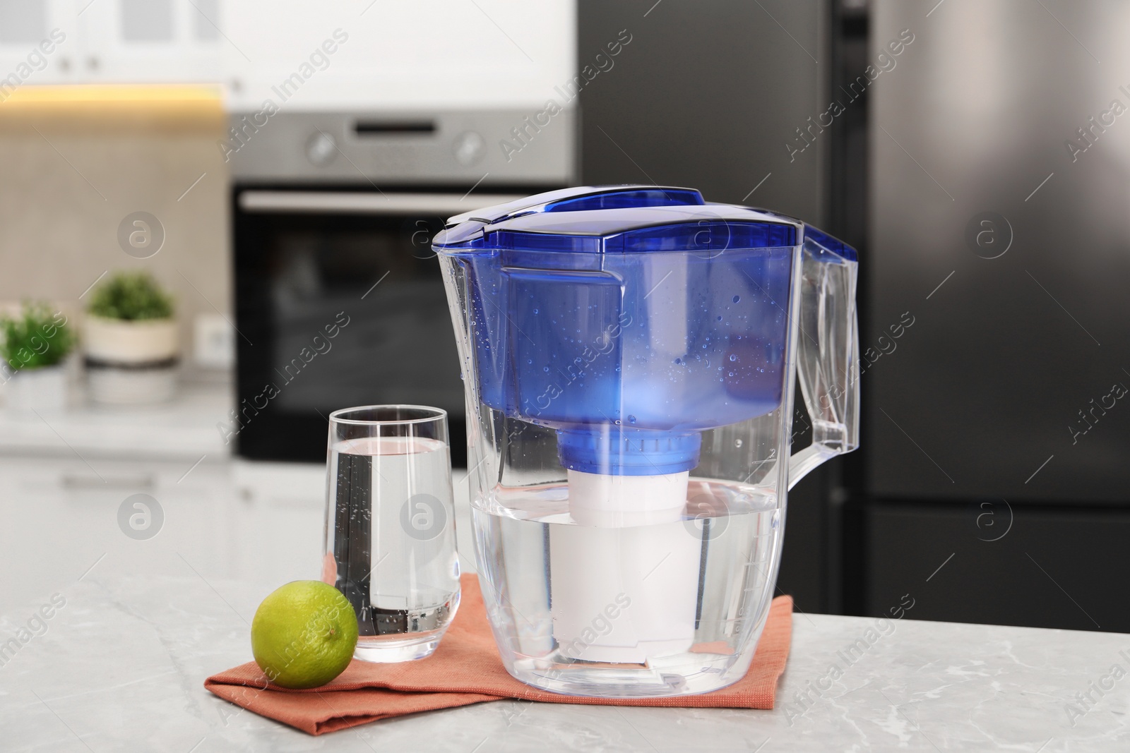 Photo of Water filter jug, glass and lime on light marble table in kitchen, closeup