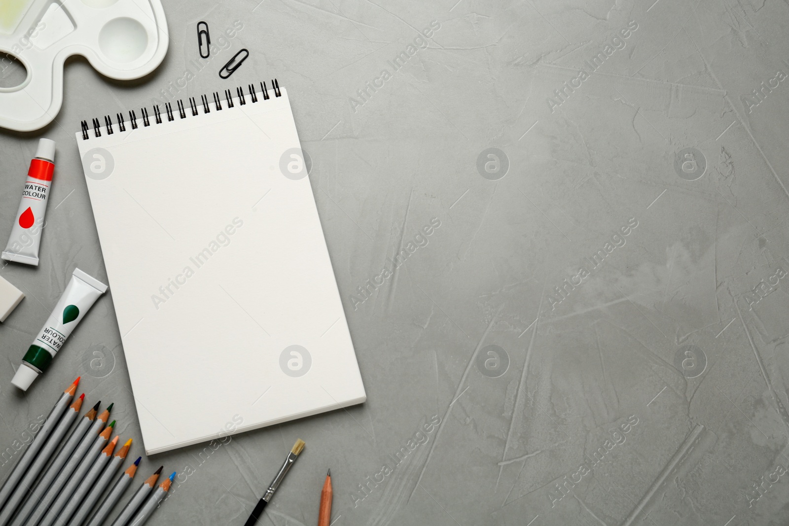 Photo of Flat lay composition with blank sketchbook on light grey stone table. Space for text