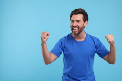 Photo of Emotional sports fan celebrating on light blue background, space for text
