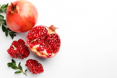 Photo of Fresh pomegranates and green leaves on white background, flat lay. Space for text