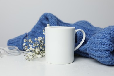 Photo of Ceramic mug, blue knitted sweater, glasses and beautiful dry flowers on white table