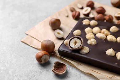 Photo of Delicious chocolate bar and hazelnuts on light grey table, closeup