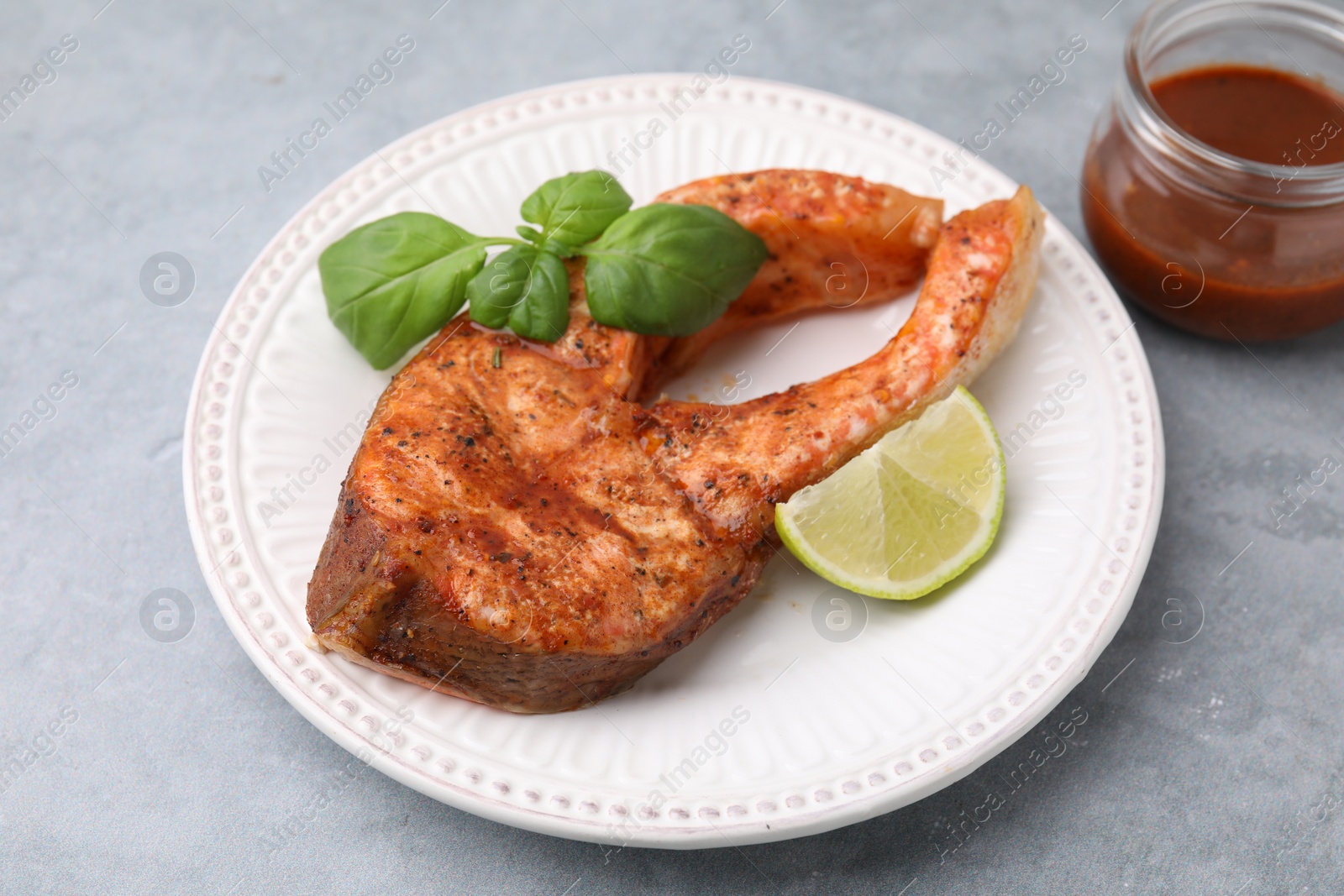 Photo of Freshly cooked fish, lime and basil on grey table