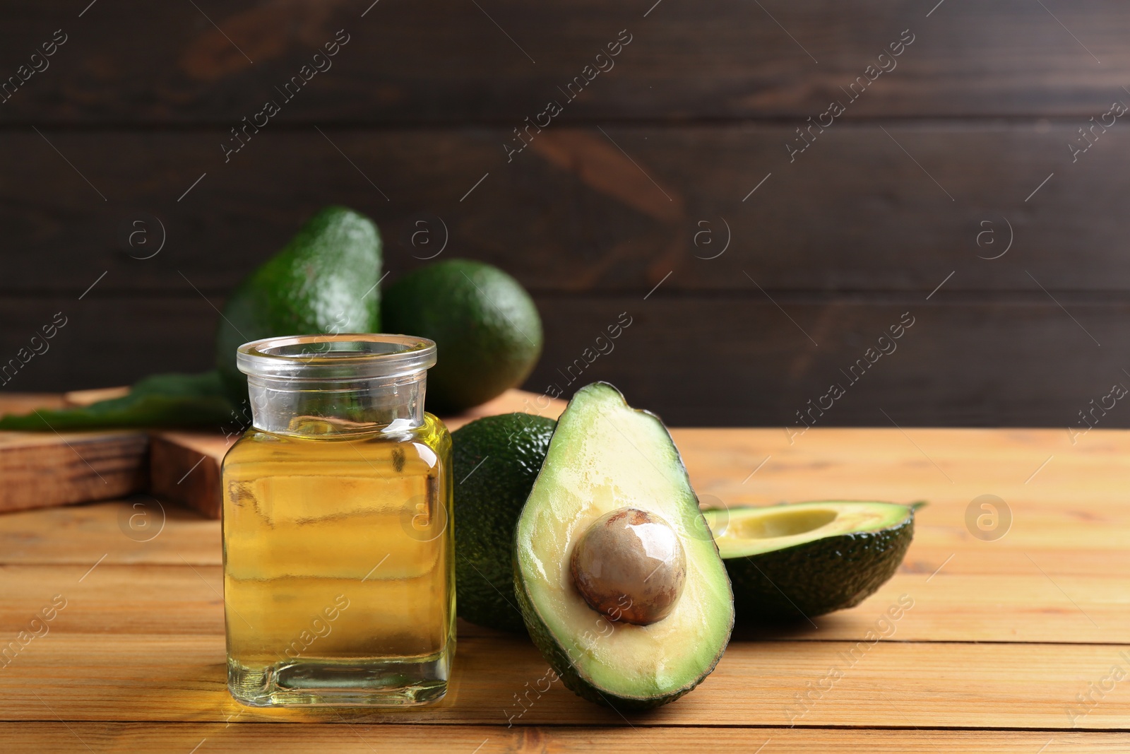 Photo of Jar of natural oil and avocados on wooden background. Space for text