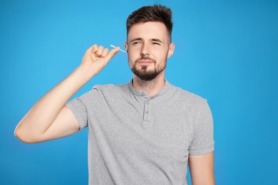 Young man cleaning ear with cotton swab on light blue background