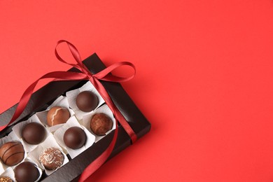 Photo of Box with delicious chocolate candies on red table, above view. Space for text