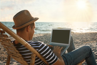 Photo of Man working with laptop in deck chair on beach