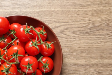 Plate with fresh cherry tomatoes on wooden background, top view. Space for text