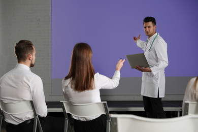 Male doctor with laptop giving lecture in conference room with projection screen