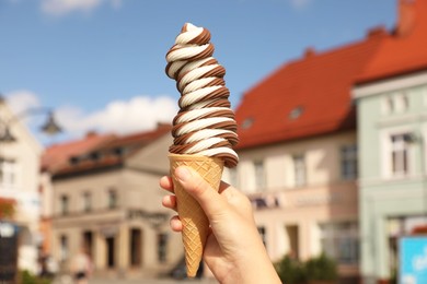 Photo of Woman holding delicious ice cream cone in city, closeup