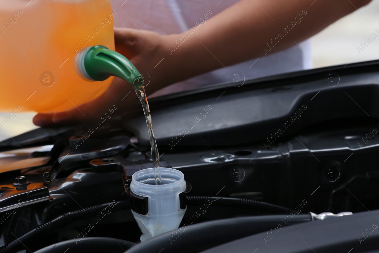 Photo of Man pouring liquid from plastic canister into car washer fluid reservoir, closeup