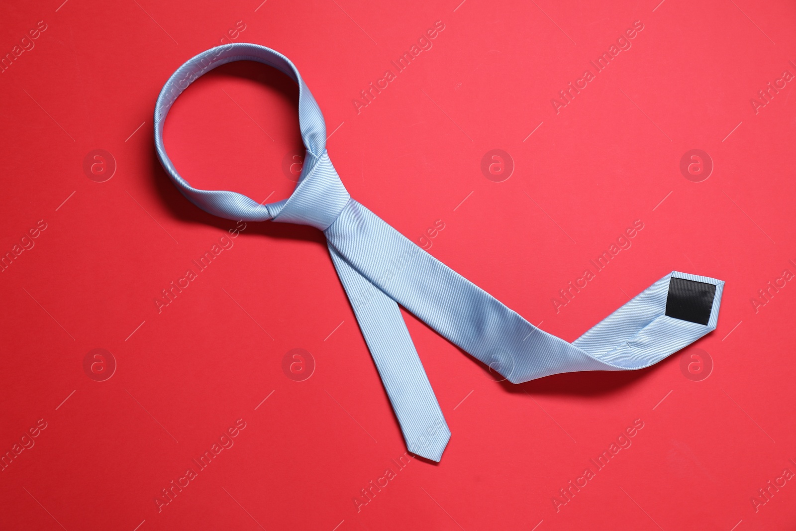 Photo of Light blue necktie on red background, top view