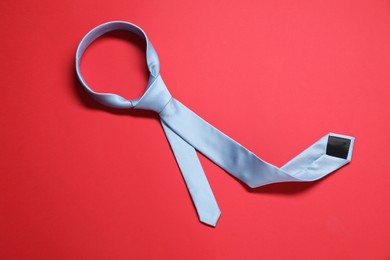 Photo of Light blue necktie on red background, top view