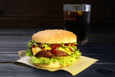 Photo of Burger with delicious patty and soda drink on black wooden table