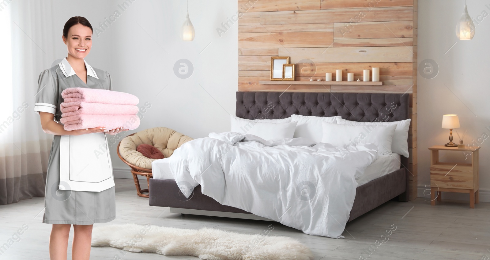 Image of Beautiful chambermaid with clean folded towels near bed in hotel room