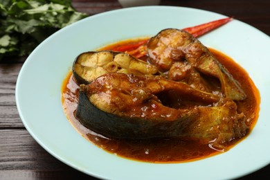 Photo of Tasty fish curry on wooden table, closeup. Indian cuisine