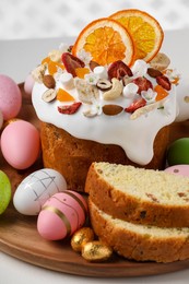 Traditional Easter cake with dried fruits and painted eggs on white table, closeup