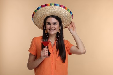 Photo of Young woman in Mexican sombrero hat with cocktail on beige background