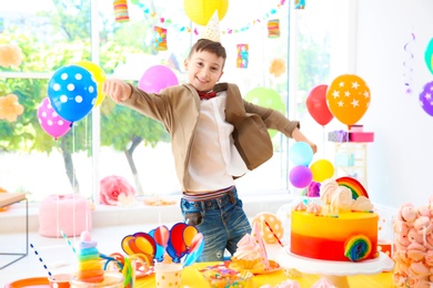 Cute little boy near table with treats at birthday party indoors