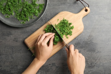 Photo of Woman cutting fresh green parsley on wooden board, top view