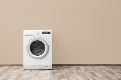 Photo of Modern washing machine with laundry near color wall, space for text