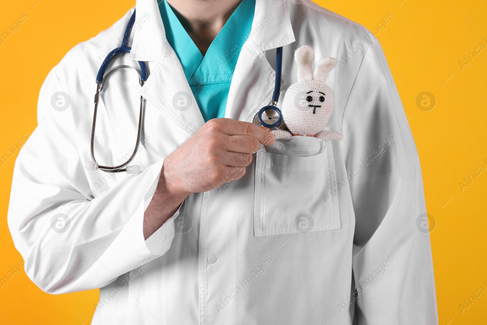 Photo of Pediatrician with toy bunny and stethoscope on yellow background, closeup