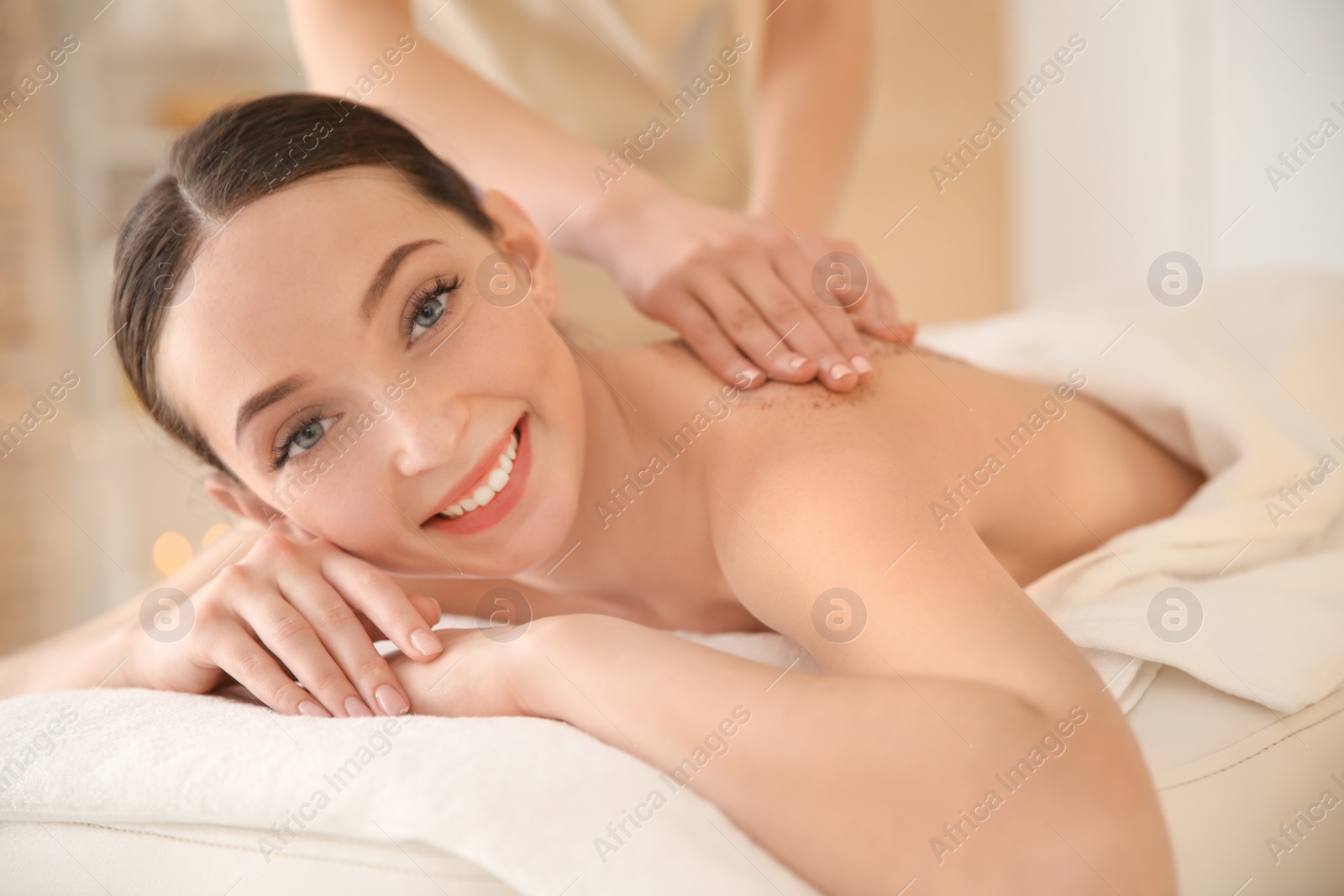 Photo of Beautiful young woman having massage with body scrub in spa salon