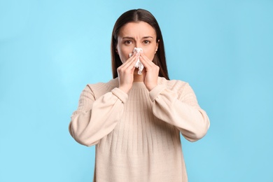 Photo of Young woman with tissue suffering from runny nose on light blue background