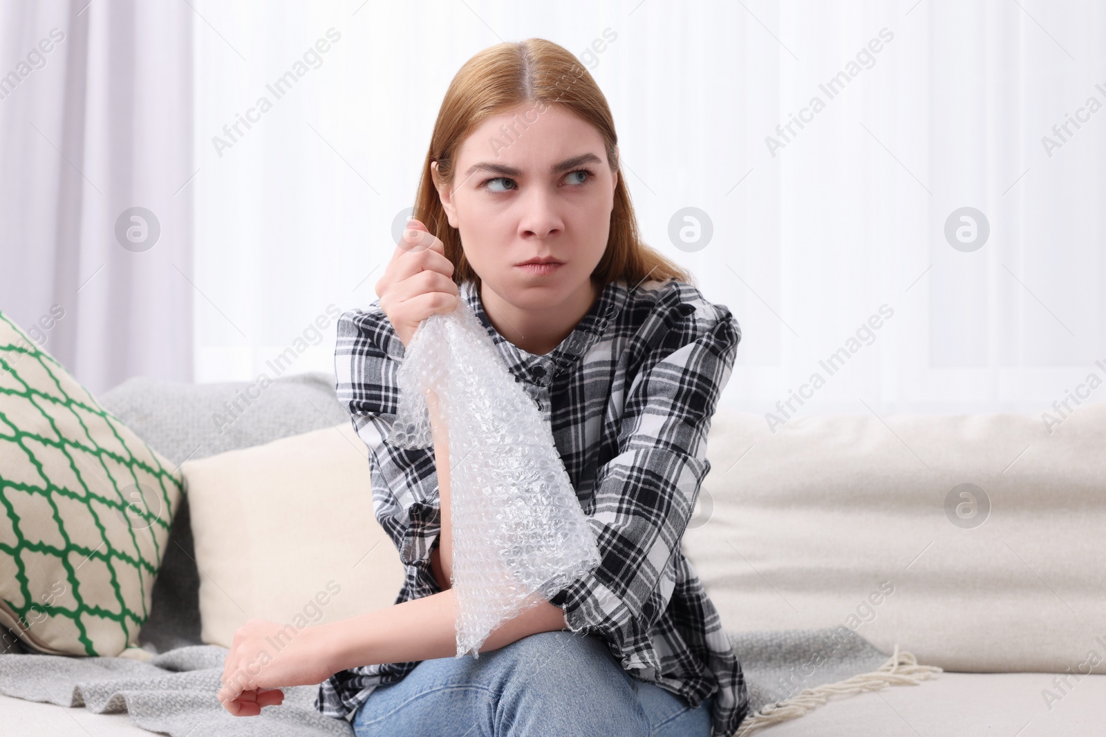 Photo of Angry woman popping bubble wrap on sofa at home. Stress relief