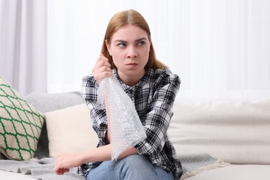 Photo of Angry woman popping bubble wrap on sofa at home. Stress relief