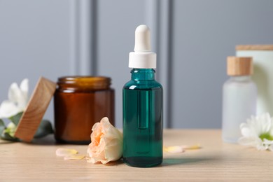Photo of Bottle of cosmetic serum, beauty products and flowers on wooden table, closeup