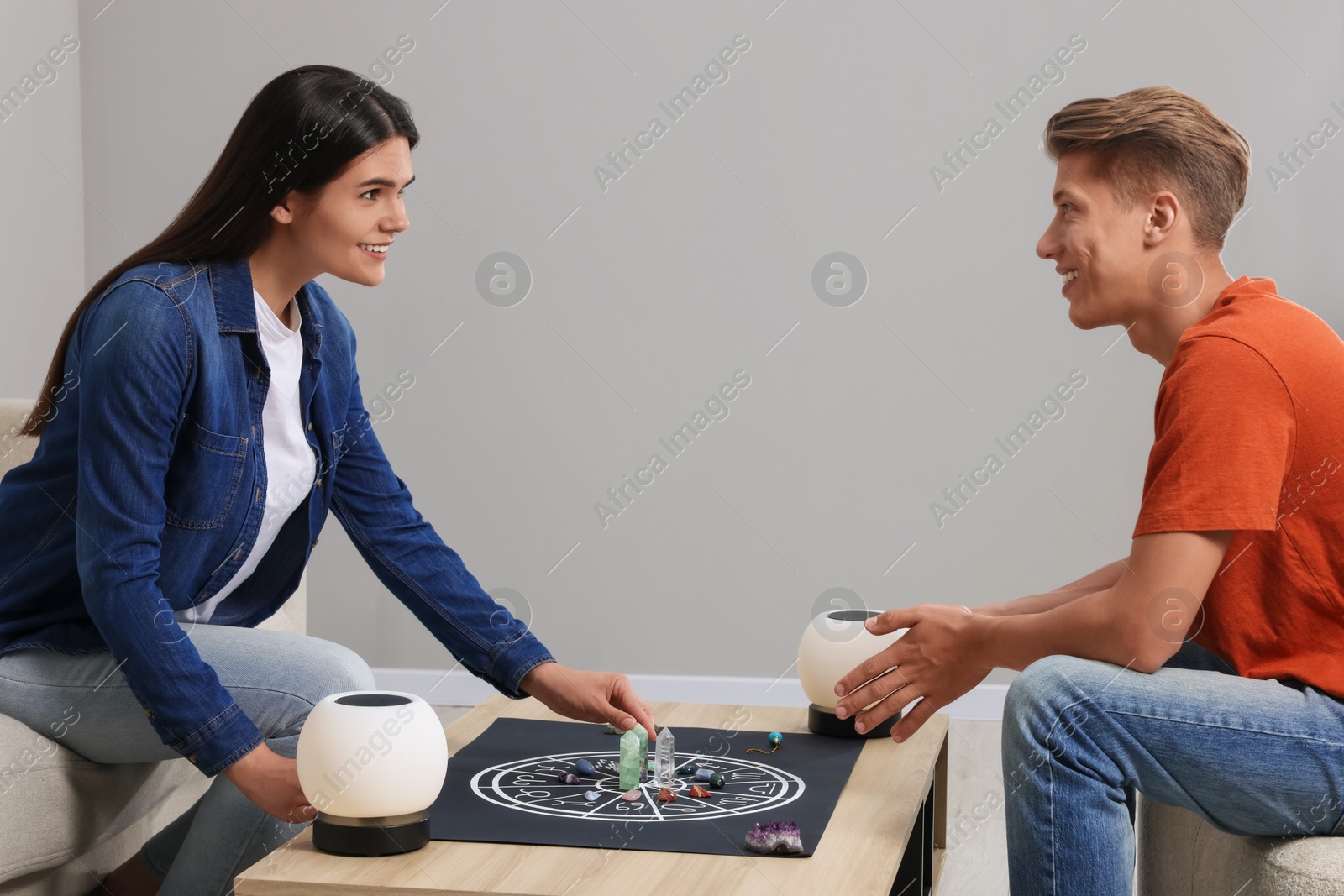 Photo of Astrologer predicting client's future with zodiac wheel, stones and crystals at wooden table indoors