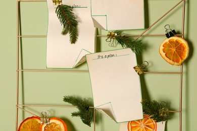 Photo of Christmas decor made of dry orange slices, notes and fir tree branches on light green wall, closeup