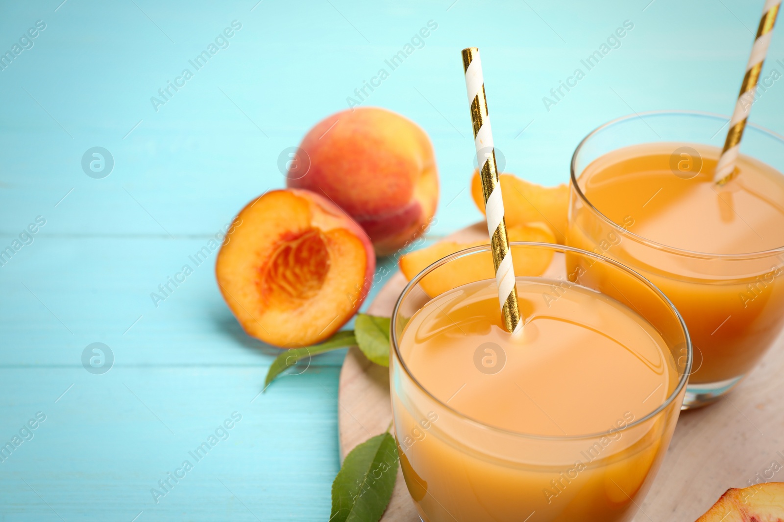 Photo of Natural peach juice and fresh fruits on light blue wooden table, closeup