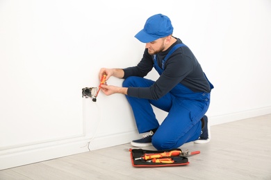 Electrician with screwdriver repairing power socket indoors